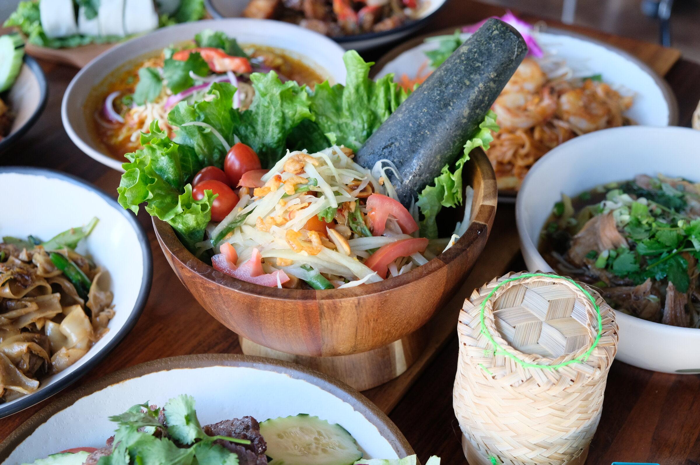 Som Tum — shredded green papaya salad in a wooden mortar with tomatoes, green beans and lettuce.