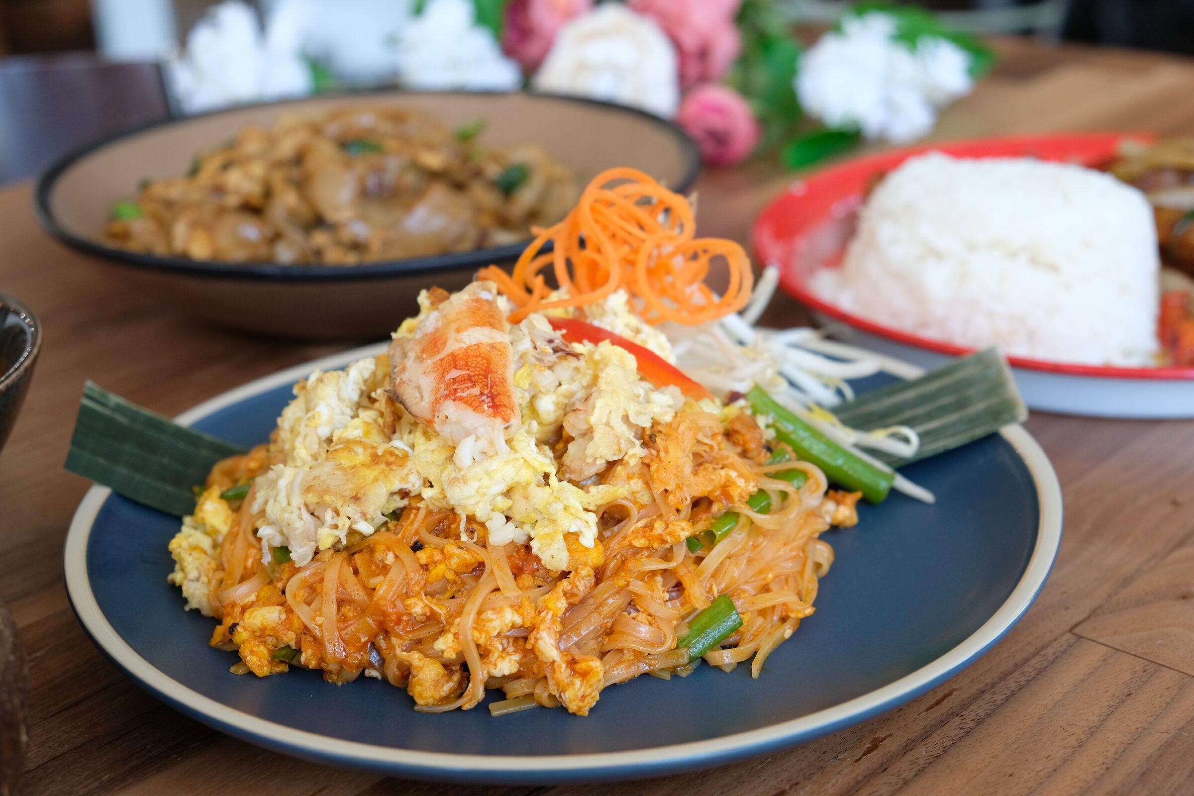 Pad Thai — pan fried rice noodles with shrimp, egg and bean sprouts on a dark plate.